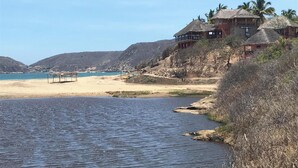 Ein Strandgrundstück mit einem Gebäude mit Strohdach, einem Sandstrand und einem ruhigen Meer.