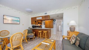Un espacio habitable compacto con comedor, sofá, cocina con armarios de madera y una pequeña zona de bar.
