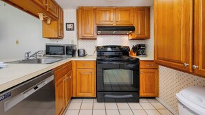 Una cocina con armarios de madera, estufa negra, microondas y lavavajillas.