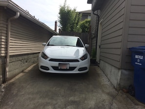 A car is parked in the driveway next to a residence with beige siding.