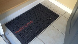 Una escalera con peldaños de madera y un felpudo negro con un mensaje de bienvenida en varios idiomas.