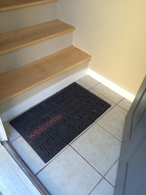 Stairs lead to a welcoming entrance with a multilingual mat.