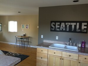 Enjoy meals in the kitchen with a granite countertop, stainless steel sink, and wooden cabinets, adjacent to a dining area with a round table and metal chairs.