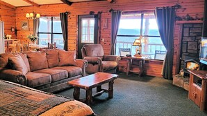 Um quarto aconchegante em estilo cabana, com sofá de couro, mesa de centro de madeira e vista para o exterior através de grandes janelas.