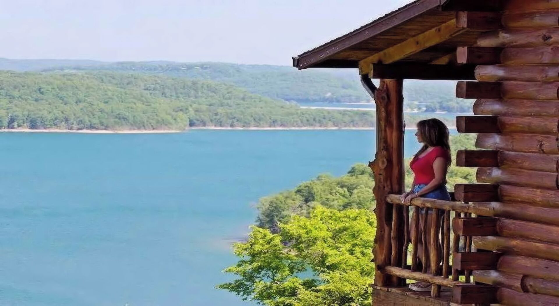 Eine Holzhütte mit einem Balkon mit Blick auf einen See und bewaldete Hügel.