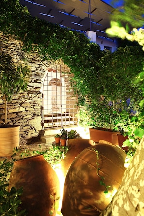 An indoor garden with stone walls, potted plants, and a metal gate.