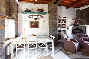 A dining area with a white table and chairs, a chandelier, a stone fireplace, and a bookshelf.
