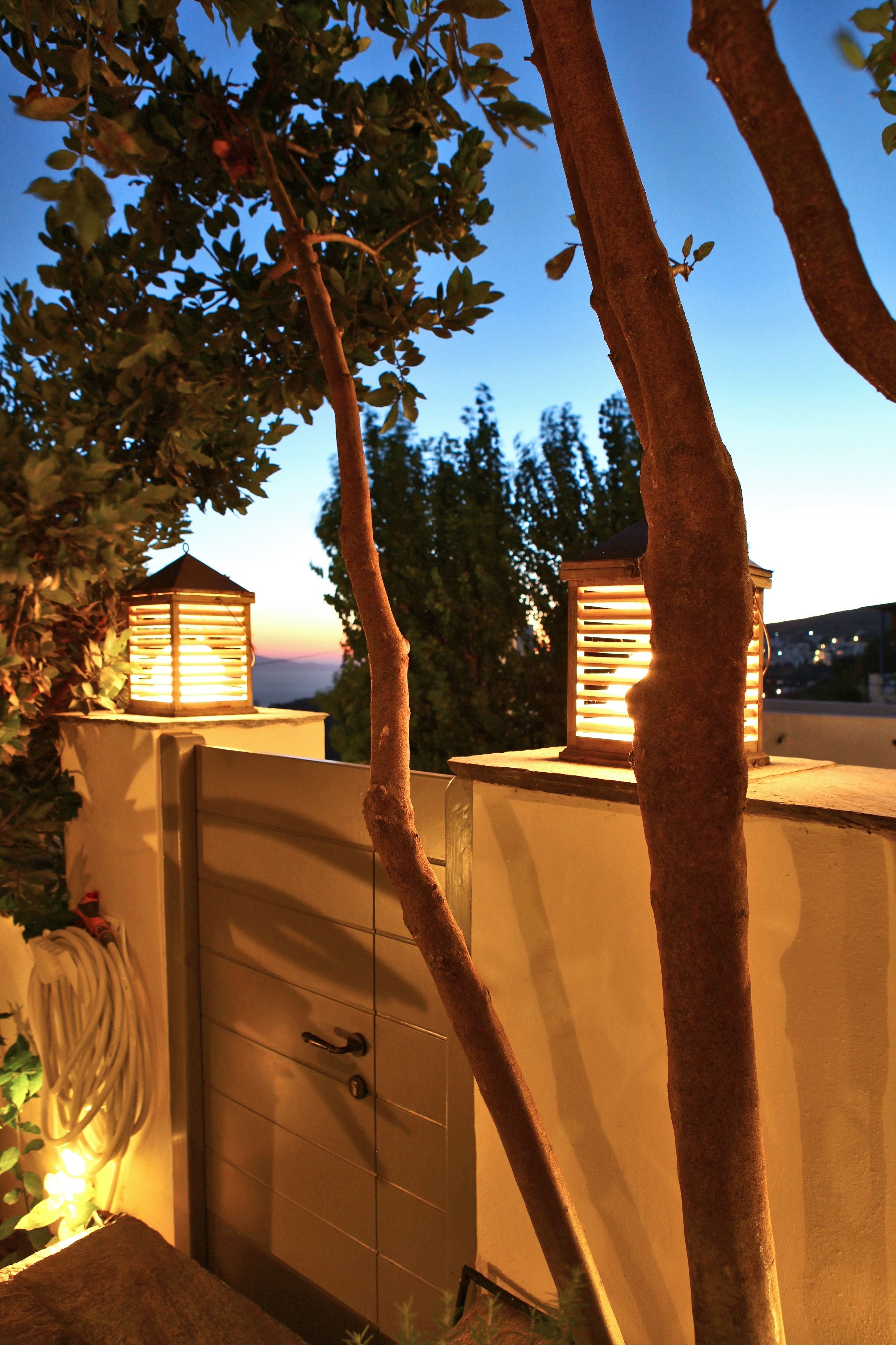 A gated area with two lantern-style lights, a metal gate, and a tree.