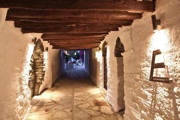 A narrow stone corridor with wooden beams overhead and white walls.