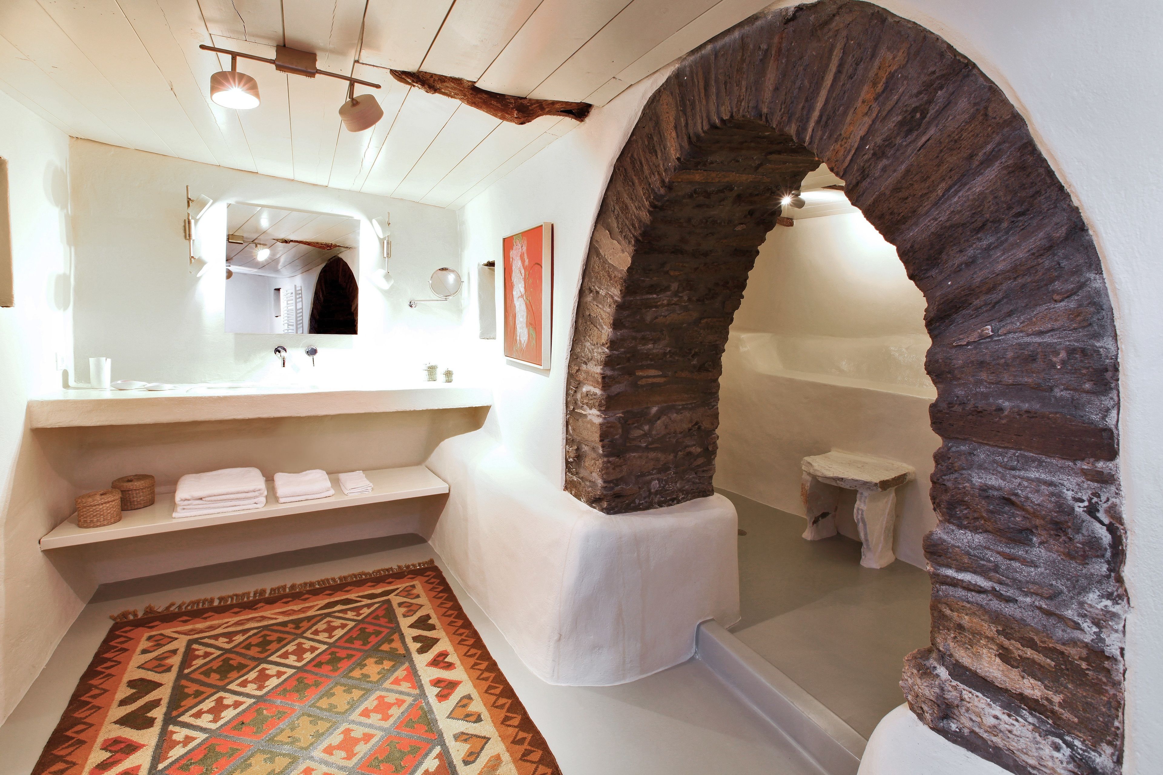 A bathroom with a stone archway, a white sink with a mirror, and a patterned rug on the floor.