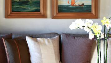 Un salon avec un canapé, une table basse sur laquelle est posée une bougie, un vase rempli de fleurs et des tableaux encadrés accrochés au mur.
