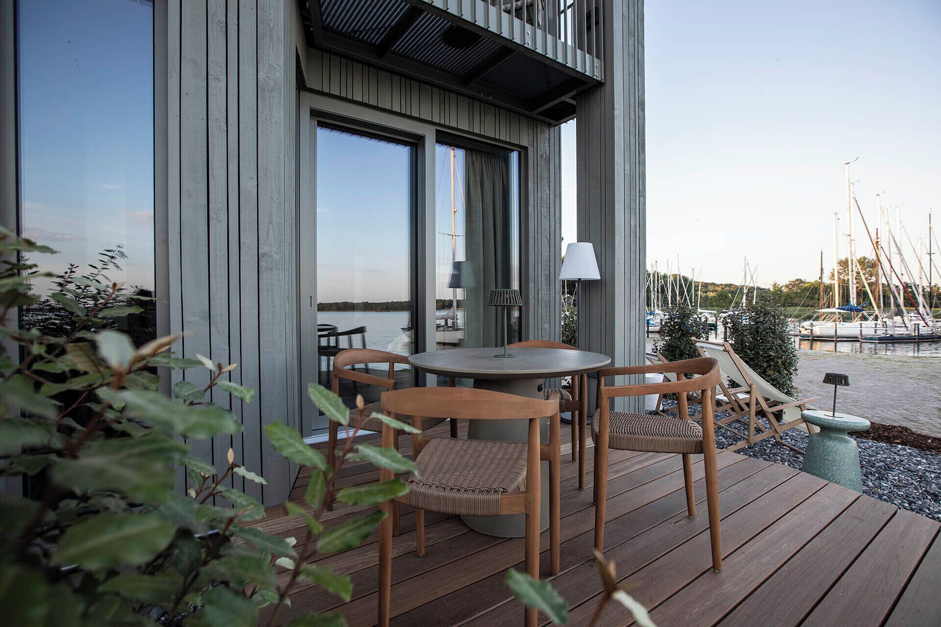 A wooden deck with a table and chairs, overlooking a marina with boats.