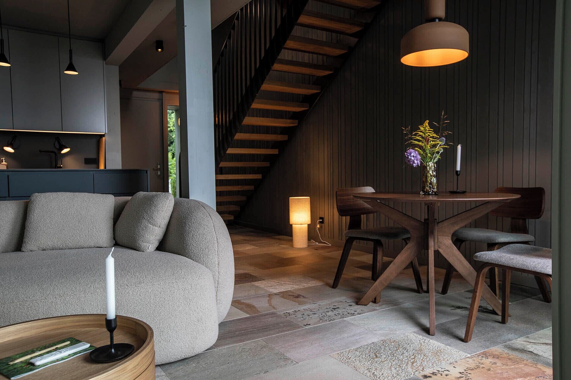 Ein modernes Interieur mit einer Couch, einem Esstisch, Stühlen, Holzbalken und einer Treppe.