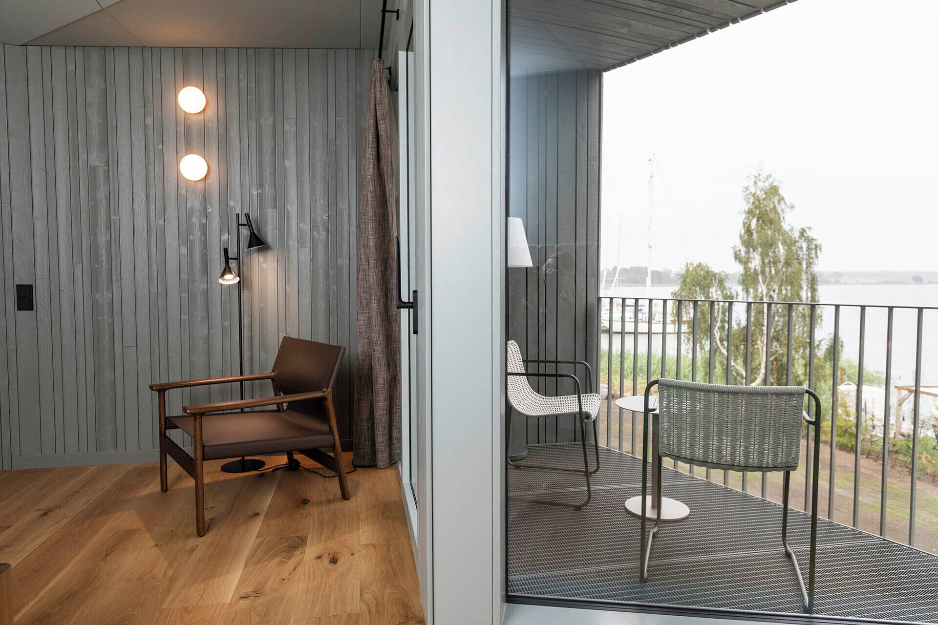 Une pièce avec un plancher en bois, une chaise marron et un balcon avec une chaise blanche et une table.