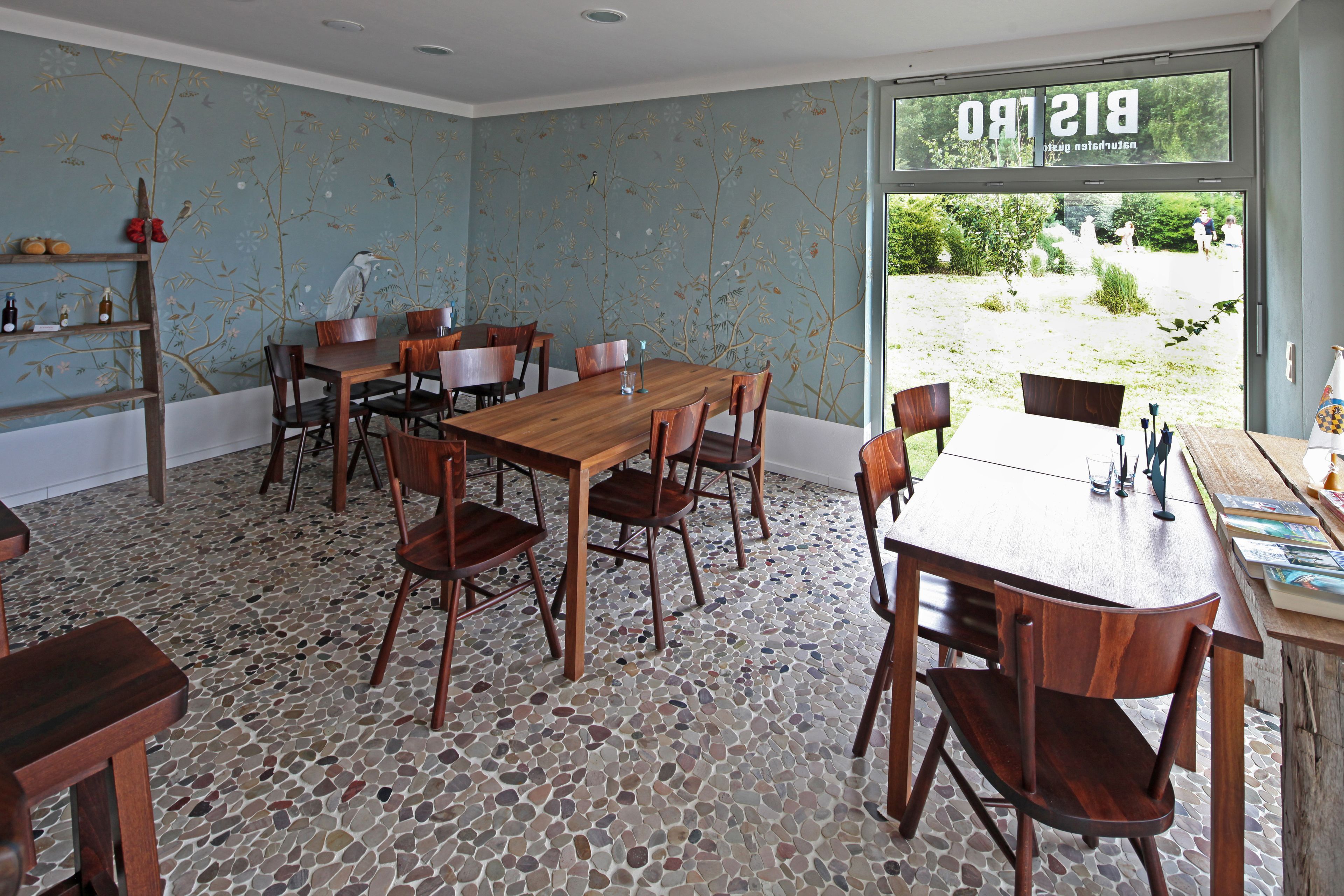A dining area with a wooden table and chairs, a mosaic floor, and a window with a view of greenery.