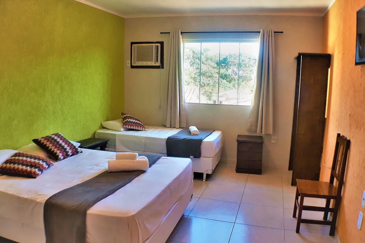 Une chambre d’hôtel avec deux lits, une télévision, une fenêtre avec des rideaux et une chaise en bois.