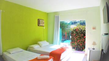 A room with two beds, a small table with a lamp, and a view of greenery outside.