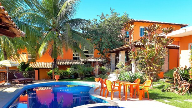 A swimming pool with two hot tubs, surrounded by orange buildings and tropical plants. - Pousada Destino Buzios (Búzios)