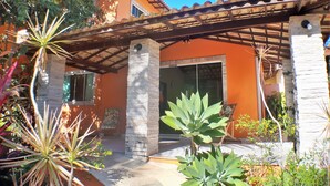 A house with a tiled roof, a stone pillar, and a covered patio area with plants. - Pousada Destino Buzios (Búzios)