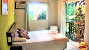 A bedroom with a bed, pillows, a bedside table, an air conditioning unit, and a window with curtains. - Pousada Destino Buzios (Búzios)