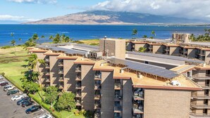 A multi-story hotel with a rooftop garden and solar panels, overlooking a coastal area with a view of the ocean and a distant mountain. - Penthouse Oceanview Vistas (Kihei, Maui)
