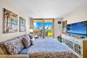 A hotel room with a bed, a TV, and a balcony with a view of the beach. - Penthouse Oceanview Vistas (Kihei, Maui)