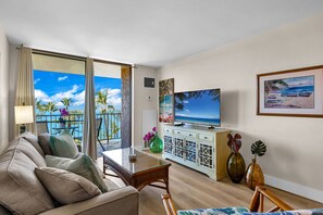 A hotel room with a balcony, a sofa, a TV, and decorative items. - Penthouse Oceanview Vistas (Kihei, Maui)
