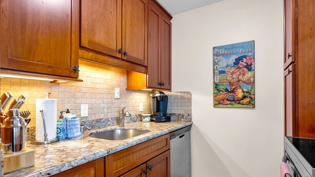 A kitchen with wooden cabinets, a marble countertop, a coffee maker, and a Hawaiian-themed poster.