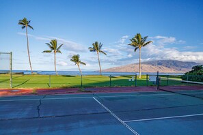 A tennis court with a net, surrounded by a fence, and palm trees in the background. - Penthouse Oceanview Vistas (Kihei, Maui)