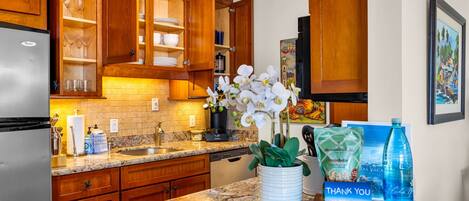 Una cocina con armarios de madera, encimera de granito, refrigerador y un florero con flores blancas.