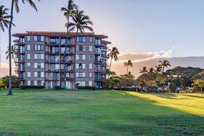 A multi-story hotel with balconies, a grassy lawn, and palm trees. - Penthouse Oceanview Vistas (Kihei, Maui)