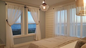 A bedroom with a bed, a view of the ocean, and a hanging light fixture.