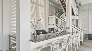 Eine moderne Küche mit einer langen Kücheninsel, weißen Barhocker und einer Treppe, die in ein Obergeschoss führt.
