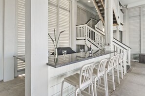 A modern kitchen with a long island counter, white bar stools, and a staircase leading to an upper level.
