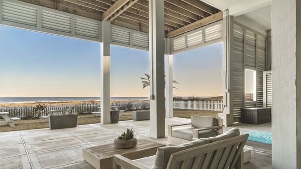 Eine überdachte Terrasse im Freien mit Blick auf den Strand, mit einer hölzernen Bank, einem kleinen Tisch und einem Blumentopf.