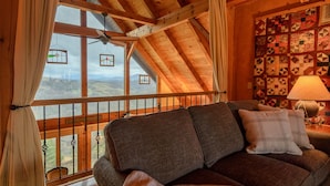 Ein gemütliches Zimmer mit Holzboden, einem großen Fenster mit Aussicht, einer Wand mit Muster und einer Couch mit Kissen.