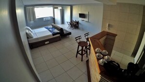 Une chambre d’hôtel moderne équipée d’un lit, d’un canapé, d’un coin repas avec des chaises, d’un téléviseur fixé au mur et d’un plan de travail de cuisine avec un service à thé.