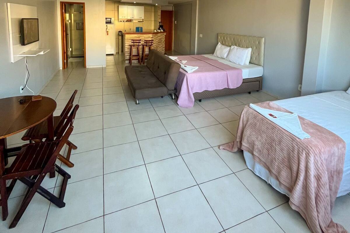 Une chambre d’hôtel avec un lit, un canapé, une table à manger avec des chaises et, au fond, une petite cuisine.