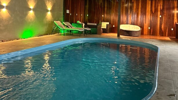 Une piscine extérieure à bords incurvés, entourée de chaises longues et d’une terrasse en bois.