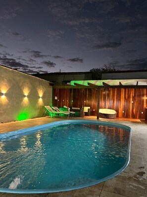 Una piscina exterior de borde curvo, rodeada de sillones de descanso y una terraza de madera.