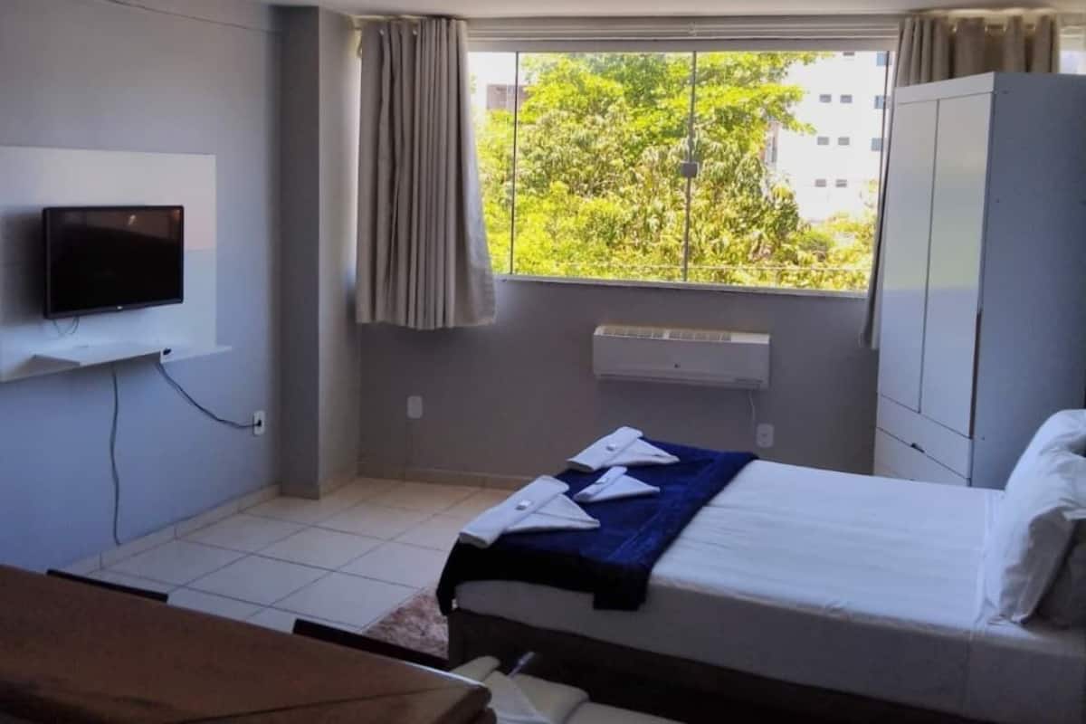 Une chambre d’hôtel avec un lit, un téléviseur fixé au mur, une fenêtre avec des rideaux et une armoire.