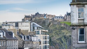 A historic castle on a cliff overlooking a modern cityscape with stone buildings and a flag. - 5* Luxury Suite Central Edinburgh stunning views of Edinburgh Castle! (Edinburgh)