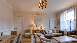 A spacious living room with a large wooden dining table, multiple sofas, a chandelier, and a large mirror. - 5* Luxury Suite Central Edinburgh stunning views of Edinburgh Castle! (Edinburgh)