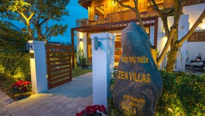 Une villa de style zen, dotée d’un portail en bois, d’un grand rocher orné d’inscriptions et d’une entrée bien éclairée.