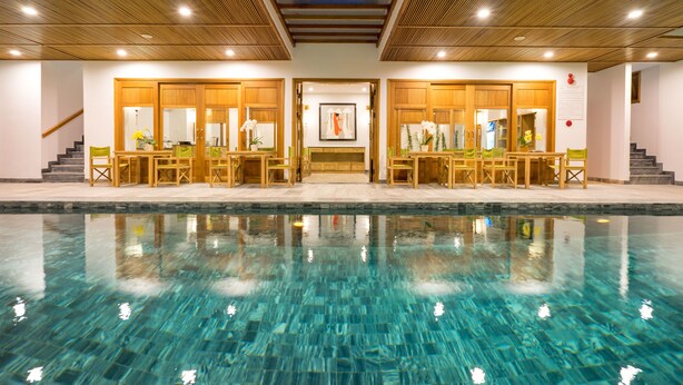 Une piscine à l’eau claire, des chaises longues en bois et un plafond en bois agrémenté d’une lucarne.