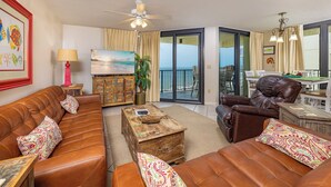 Ein Wohnzimmer mit einer Couch, einem Sessel, einem Couchtisch und einem Fernseher, der eine Strandansicht zeigt.