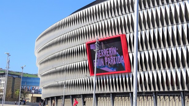 Ein modernes Gebäude mit einer markanten, gerippten Fassade und einer großen digitalen Werbetafel mit Text.