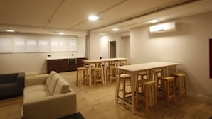 Une pièce spacieuse avec une longue table et plusieurs chaises, un canapé et un petit coin cuisine.