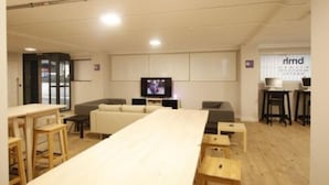 Une pièce moderne et bien éclairée, avec une longue table, un canapé et un téléviseur.