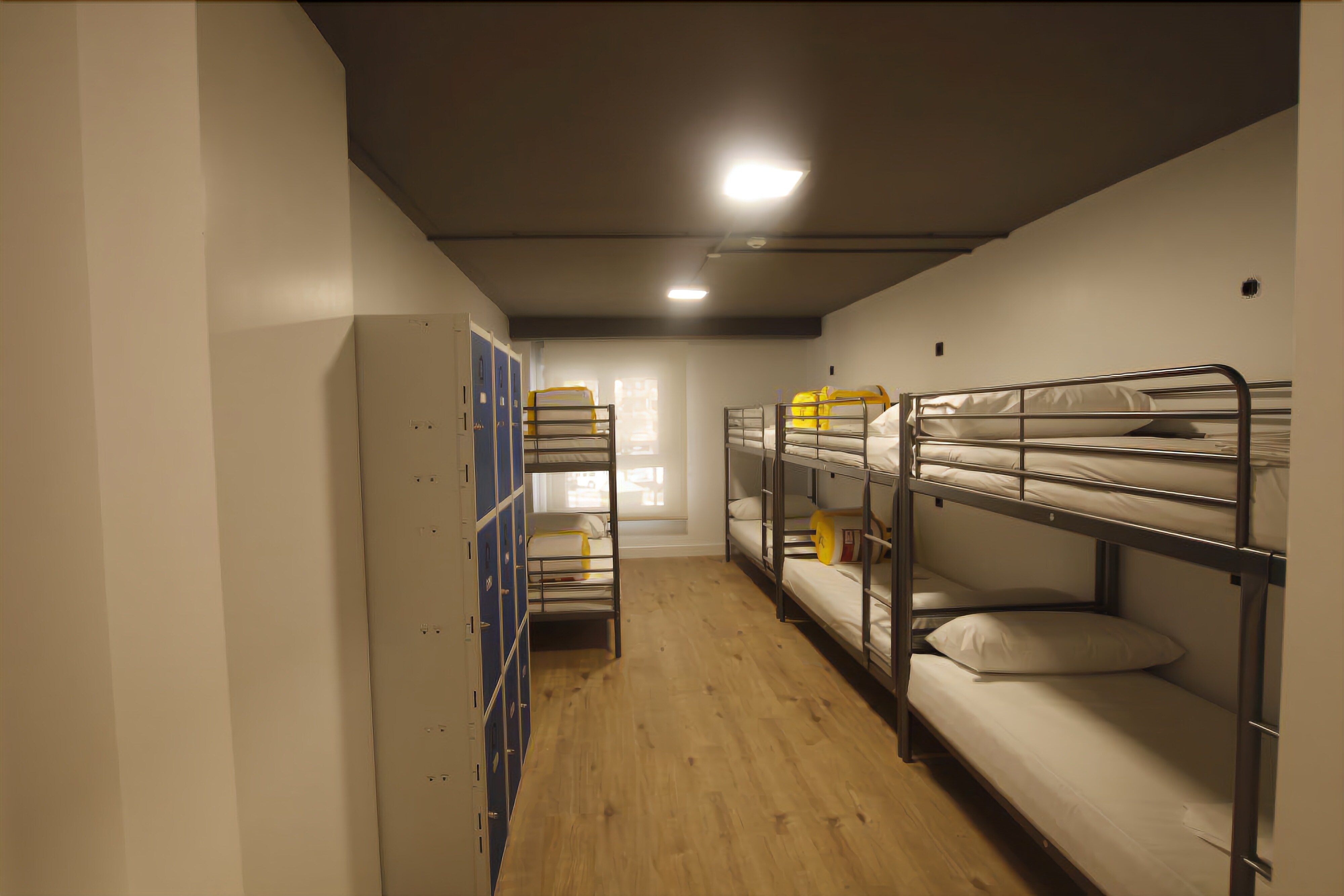 A dormitory room with bunk beds, a wardrobe, and a window with natural light.